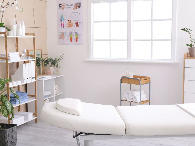 A white room with a massage table and plants, providing specialist massage therapy.